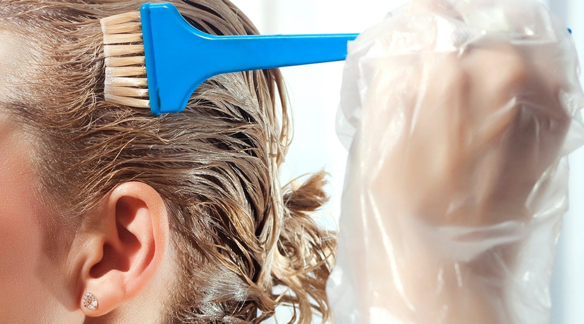 Ein Frau trägt eine Coloration mit einem Pinsel auf ihre Haare auf